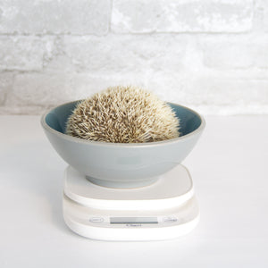 A curled up hedgehog hiding in a bowl on a white scale